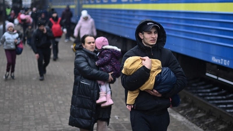 A man carries a baby as they rush to board a train taking refugees to Poland at Lviv train station, western Ukraine, on March 5, 2022. – The UN Human Rights Council on March 4, 2022, overwhelmingly voted to create a top-level investigation into v